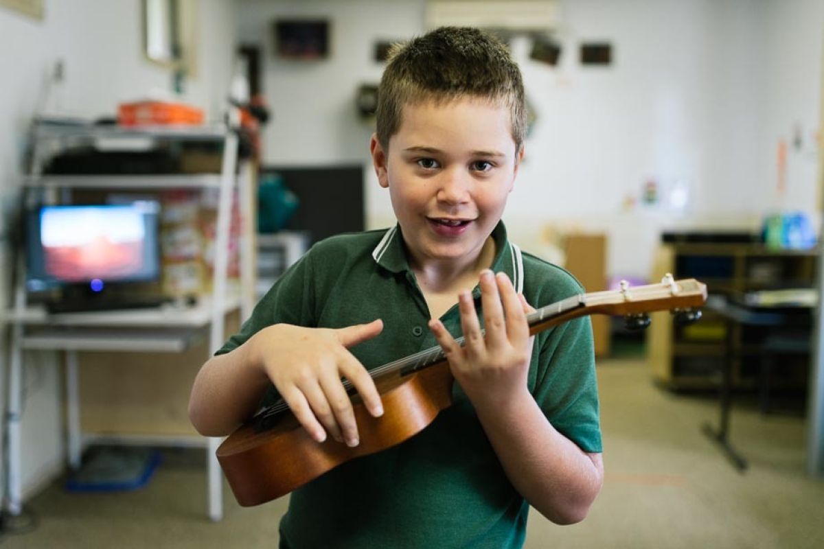 A student plays guitar in classroom at Macarthur school