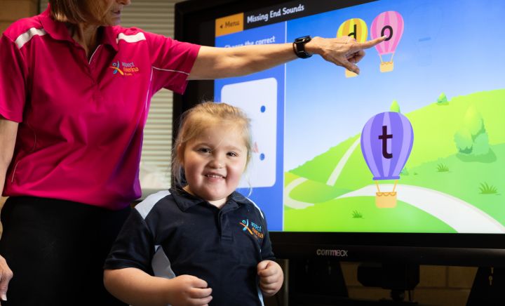 Student smiles at the camera infront of an interactive whiteboard